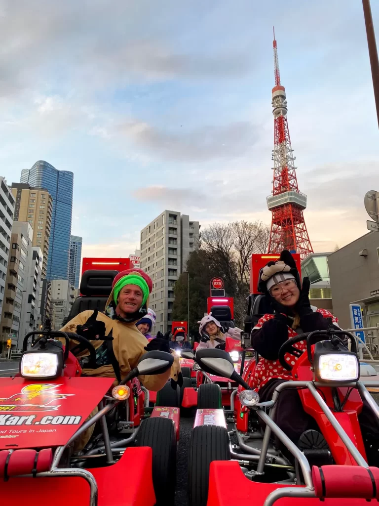 Group of people in red go-karts posing and giving thumbs up on a city street with Tokyo Tower in the background.